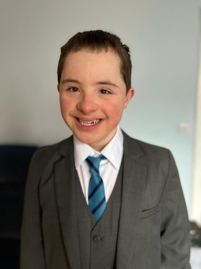 A teenage boy in a smart grey suit and blue tie smiling confidently
