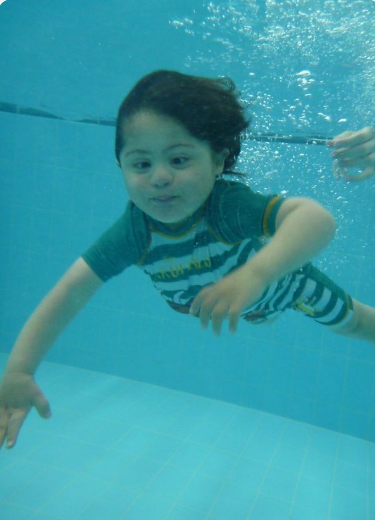 A young boy swimming underwater in a pool, arms outstretched