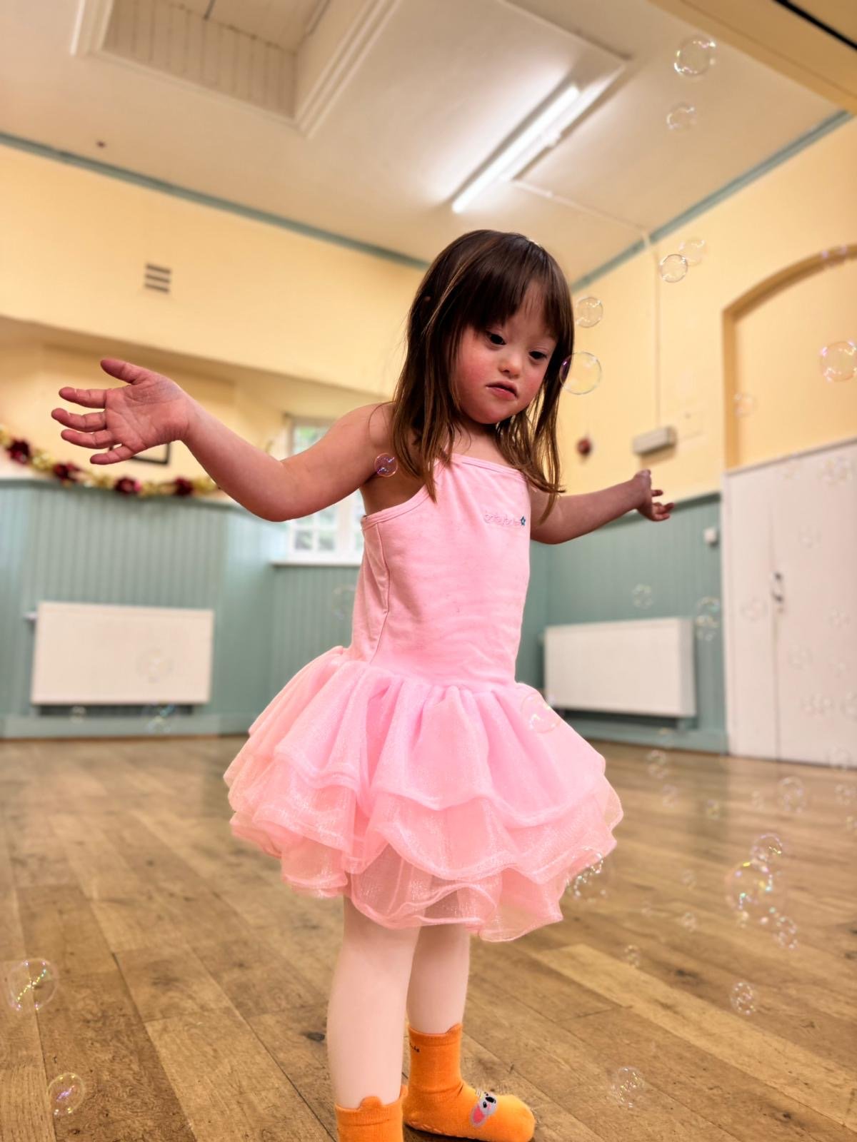 A girl in a pink tutu reaching her arms out to catch soap bubbles in a dance studio