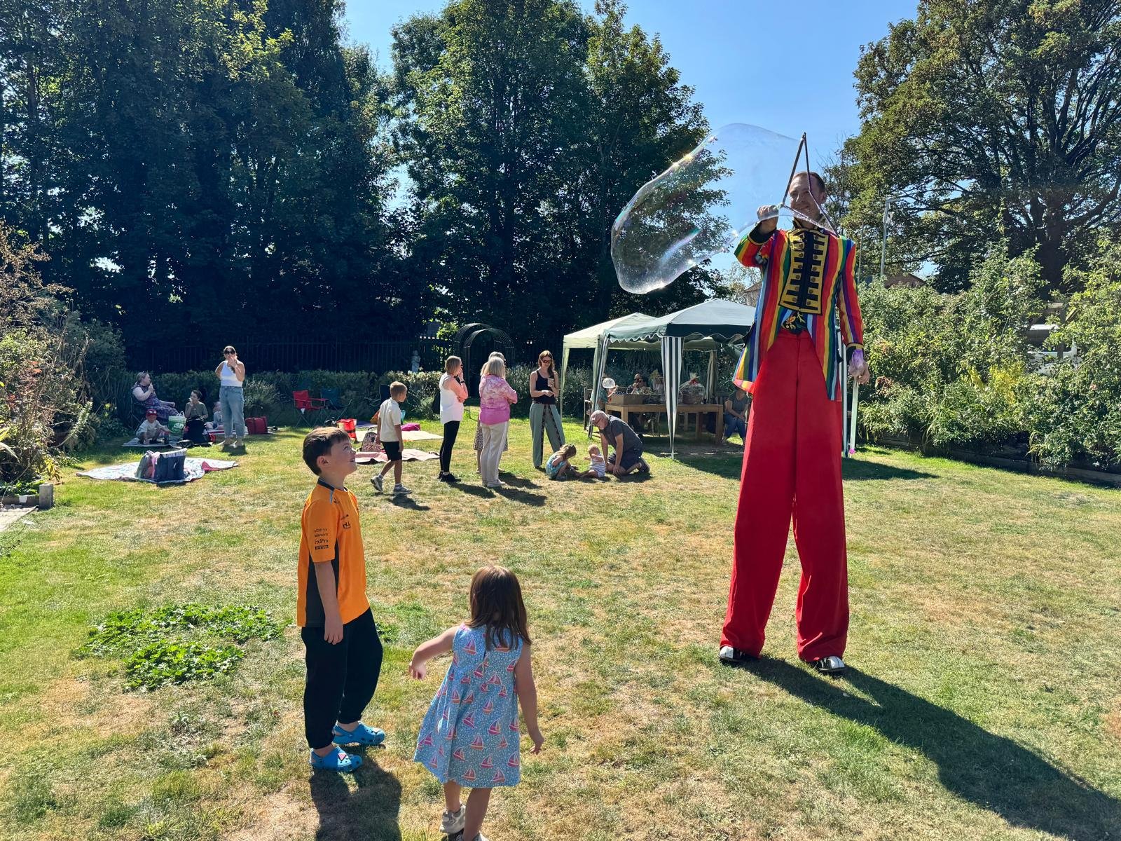 Man on stilts blowing bubbles on grass